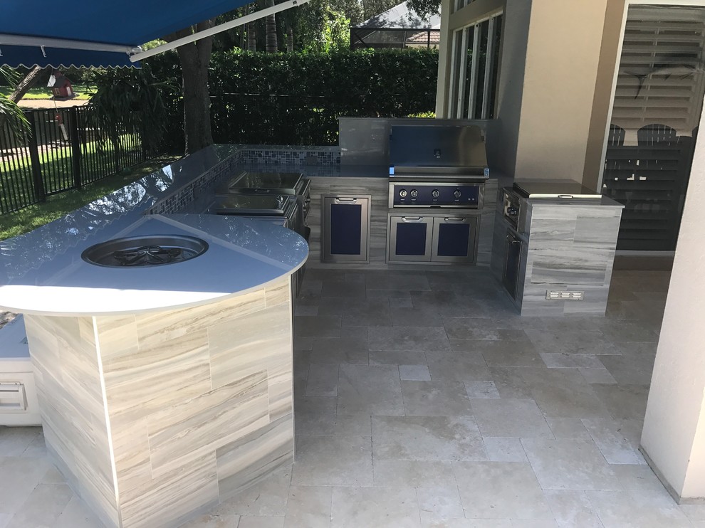 Tropical backyard patio in Miami with an outdoor kitchen, natural stone pavers and an awning.