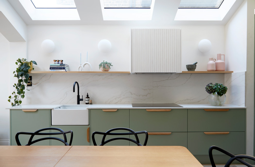 Photo of a mid-sized scandinavian galley open plan kitchen in London with a farmhouse sink, flat-panel cabinets, green cabinets, white splashback, marble splashback, black appliances, medium hardwood floors, no island, beige floor, white benchtop and quartzite benchtops.