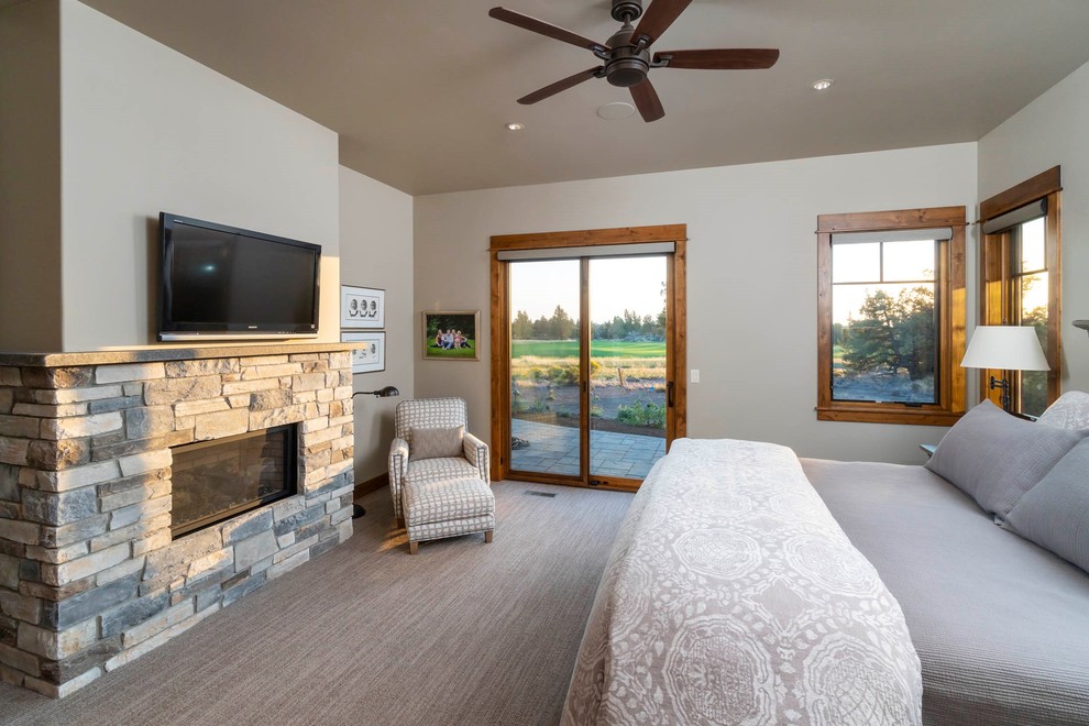 Large mountain style master carpeted and beige floor bedroom photo with beige walls, a standard fireplace and a stone fireplace