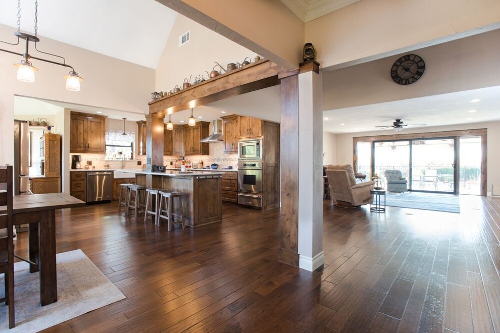 Inspiration for a large transitional l-shaped brown floor and medium tone wood floor eat-in kitchen remodel in Dallas with a farmhouse sink, recessed-panel cabinets, medium tone wood cabinets, multicolored backsplash, an island, quartzite countertops, travertine backsplash, stainless steel appliances and white countertops