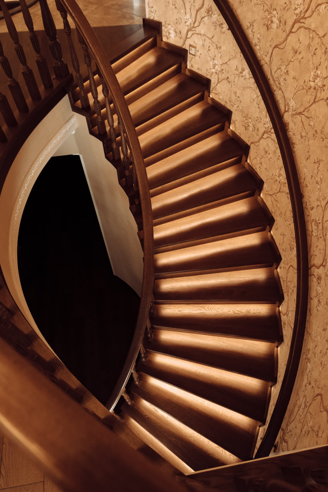 Источник вдохновения для домашнего уюта: большая изогнутая деревянная лестница в классическом стиле с деревянными ступенями, деревянными перилами, обоями на стенах и кладовкой или шкафом под ней