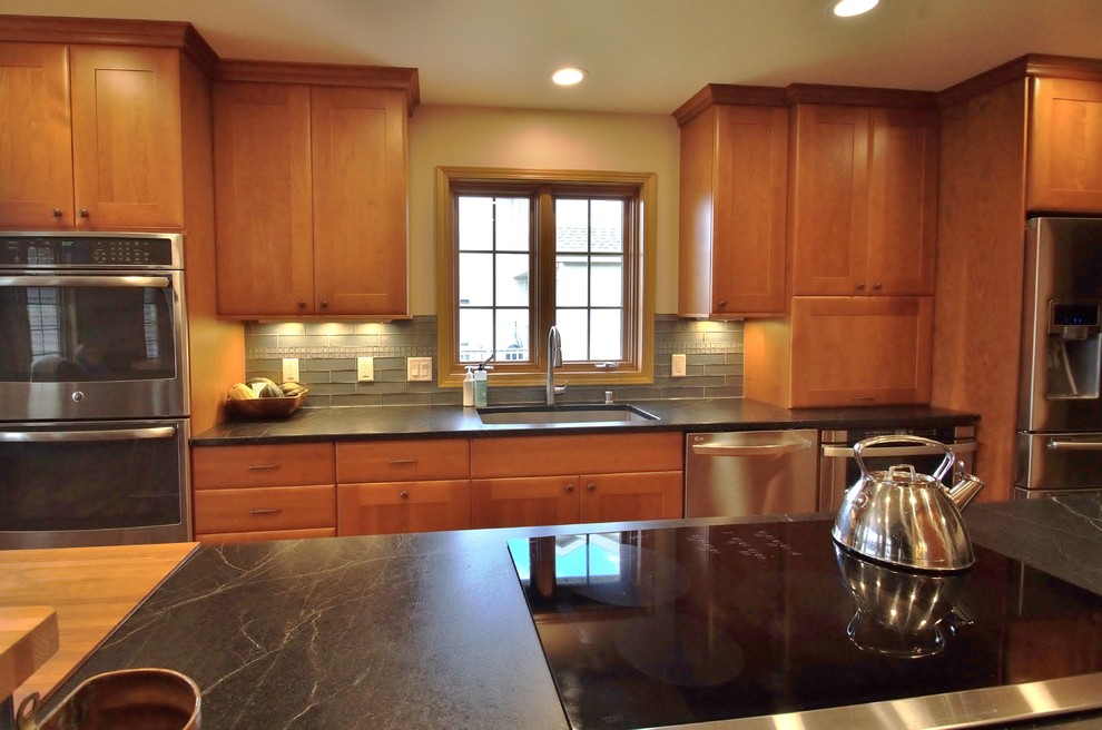 Transitional galley medium tone wood floor eat-in kitchen photo with a double-bowl sink, recessed-panel cabinets, medium tone wood cabinets, soapstone countertops, stainless steel appliances and an island