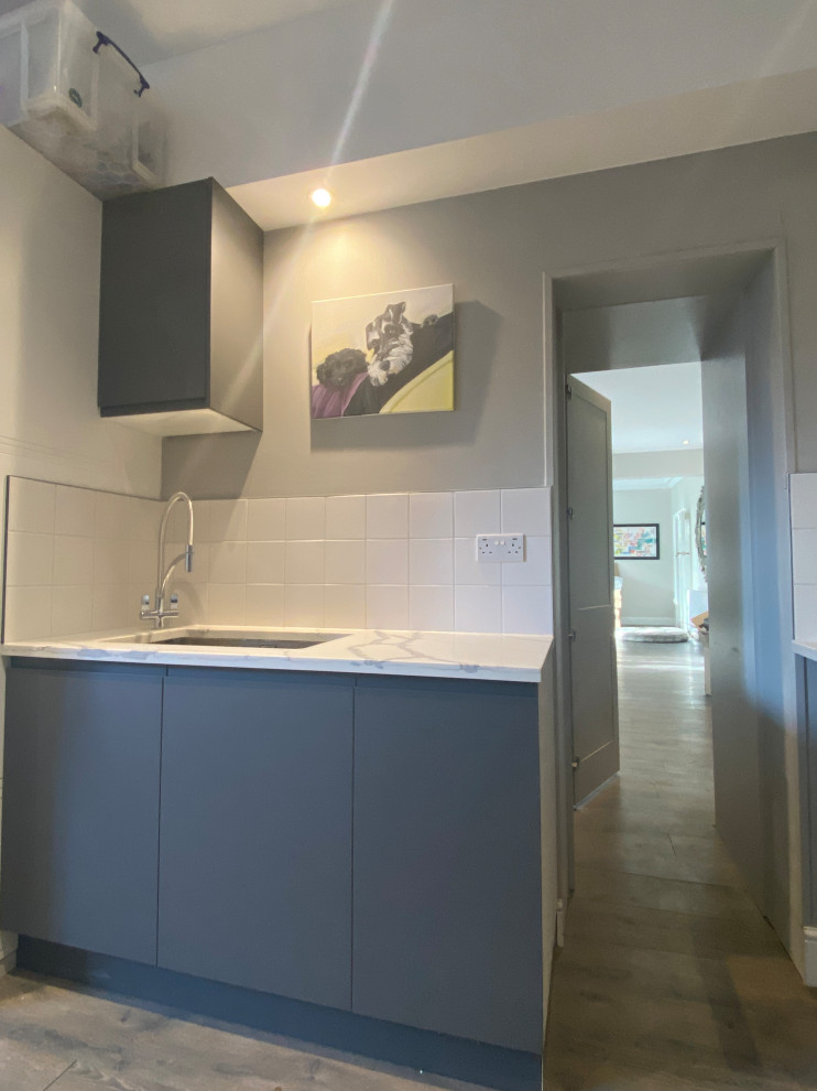 Large contemporary galley utility room in London with a built-in sink, flat-panel cabinets, grey cabinets, quartz worktops, white splashback, porcelain splashback, beige walls, laminate floors, a side by side washer and dryer, grey floors and multicoloured worktops.