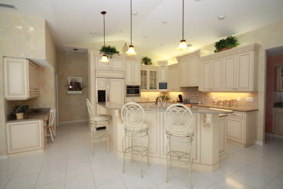 Inspiration for a large transitional l-shaped porcelain tile eat-in kitchen remodel in Tampa with beaded inset cabinets, beige cabinets, beige backsplash, stone tile backsplash, paneled appliances and an island