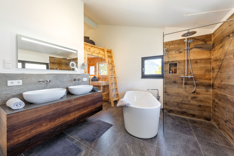 Photo of a mid-sized traditional bathroom in Munich with beaded inset cabinets, brown cabinets, a freestanding tub, a curbless shower, gray tile, brown walls, with a sauna, a vessel sink, wood benchtops, an open shower, grey benchtops, a double vanity and a floating vanity.