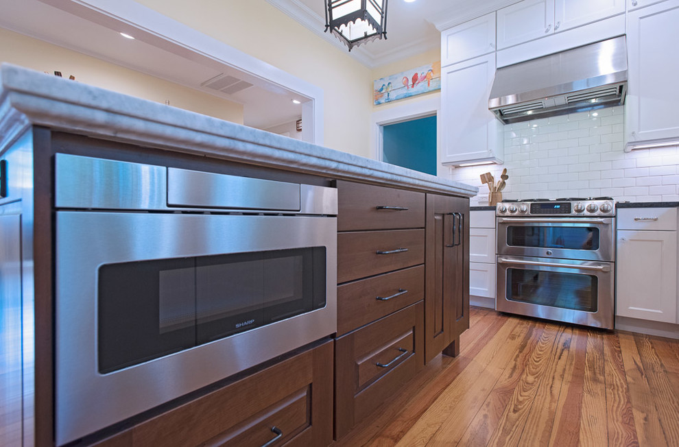 Mid-sized transitional l-shaped medium tone wood floor and brown floor enclosed kitchen photo in Austin with an undermount sink, shaker cabinets, white cabinets, granite countertops, white backsplash, subway tile backsplash, stainless steel appliances, an island and black countertops