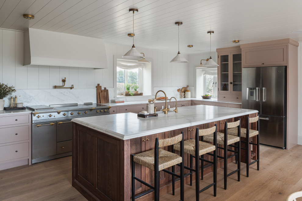 Inspiration for a mid-sized country kitchen in Other with with island, a farmhouse sink, recessed-panel cabinets, pink cabinets, granite benchtops, white splashback, granite splashback, stainless steel appliances, light hardwood floors and white benchtop.