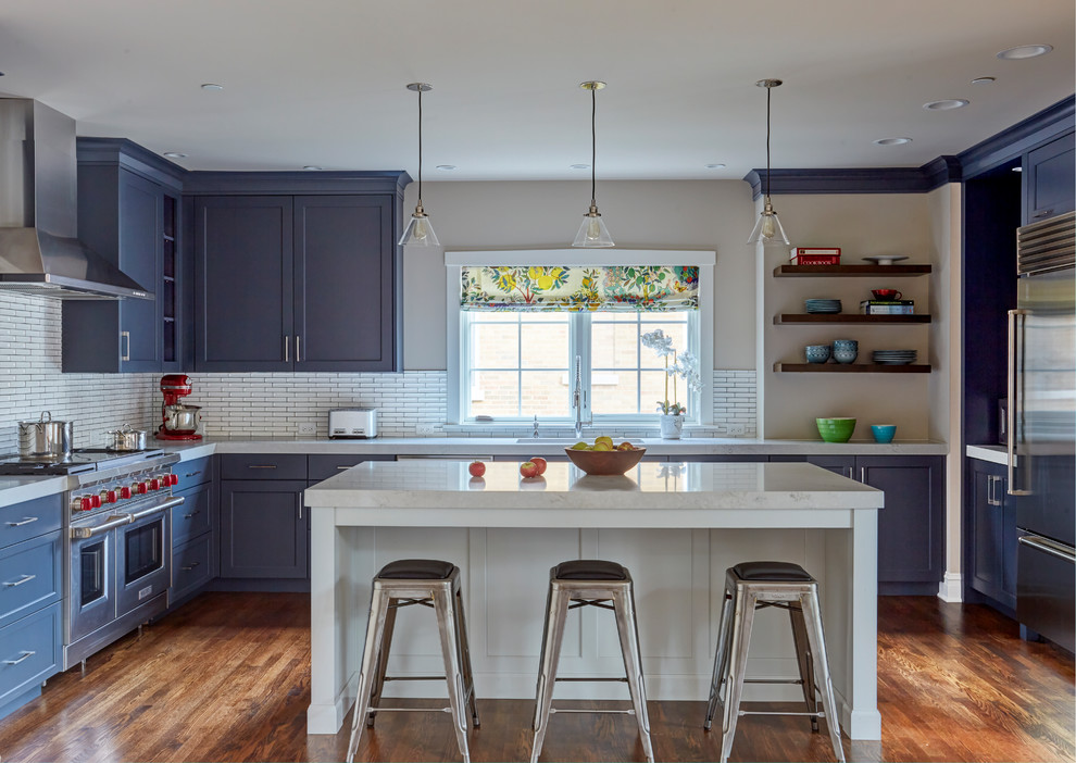 Inspiration for a mid-sized transitional u-shaped dark wood floor and brown floor kitchen remodel with an undermount sink, recessed-panel cabinets, blue cabinets, white backsplash, ceramic backsplash, stainless steel appliances, an island and white countertops