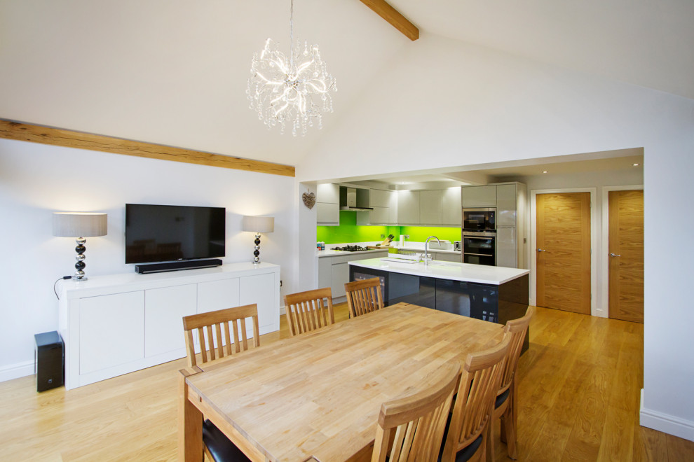 Small contemporary l-shaped open plan kitchen in West Midlands with a drop-in sink, flat-panel cabinets, grey cabinets, granite benchtops, green splashback, glass sheet splashback, stainless steel appliances, laminate floors, with island, beige floor, white benchtop and vaulted.