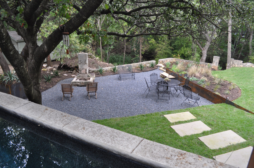 Inspiration for a large modern backyard partial sun xeriscape in Austin with a retaining wall and gravel.