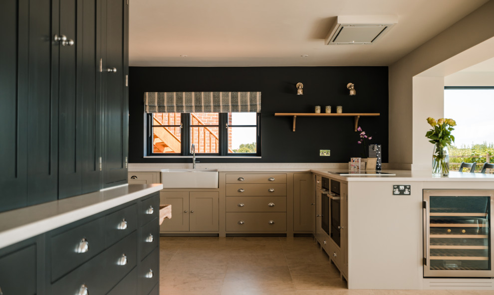 This is an example of a large beach style l-shaped eat-in kitchen in Hampshire with a farmhouse sink, shaker cabinets, grey cabinets, quartzite benchtops, white splashback, engineered quartz splashback, stainless steel appliances, limestone floors, a peninsula, beige floor and white benchtop.