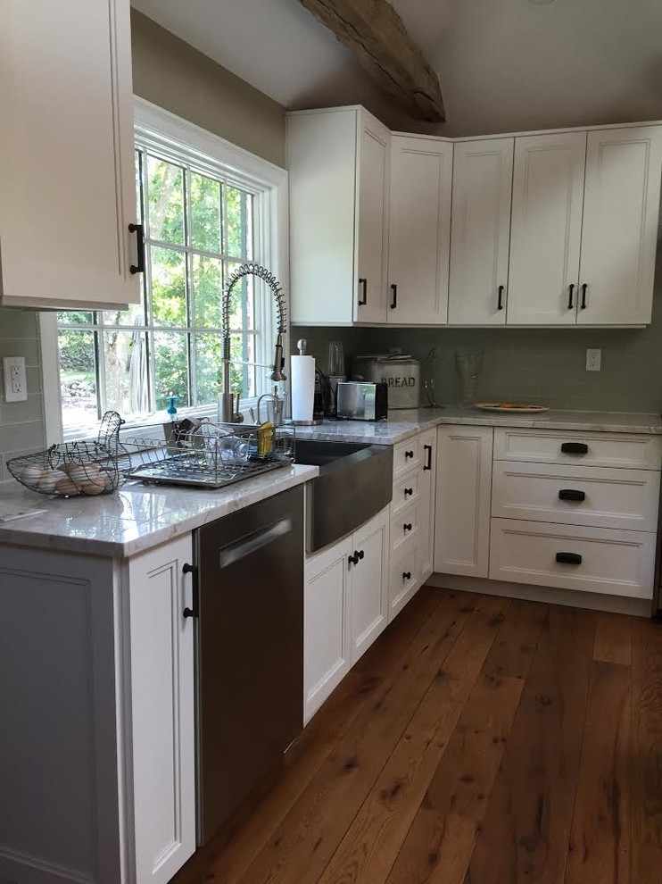 Example of a large mountain style l-shaped medium tone wood floor and brown floor open concept kitchen design in New York with a farmhouse sink, recessed-panel cabinets, white cabinets, quartz countertops, green backsplash, glass tile backsplash, stainless steel appliances and an island