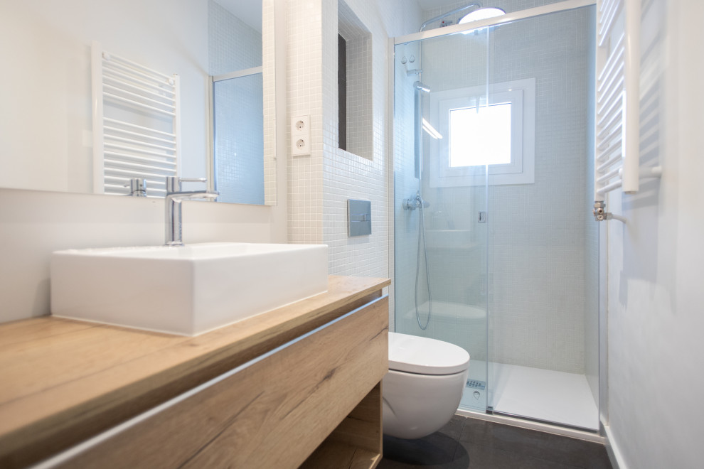 This is an example of a mid-sized mediterranean master bathroom in Barcelona with flat-panel cabinets, medium wood cabinets, a curbless shower, a one-piece toilet, white tile, ceramic tile, ceramic floors, a vessel sink, grey floor, a sliding shower screen, brown benchtops, an enclosed toilet, a single vanity and a floating vanity.