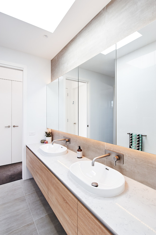 This is an example of a large contemporary master bathroom in Melbourne with flat-panel cabinets, light wood cabinets, a shower/bathtub combo, white tile, glass sheet wall, grey walls, ceramic floors, a drop-in sink, engineered quartz benchtops, grey floor, an open shower and white benchtops.