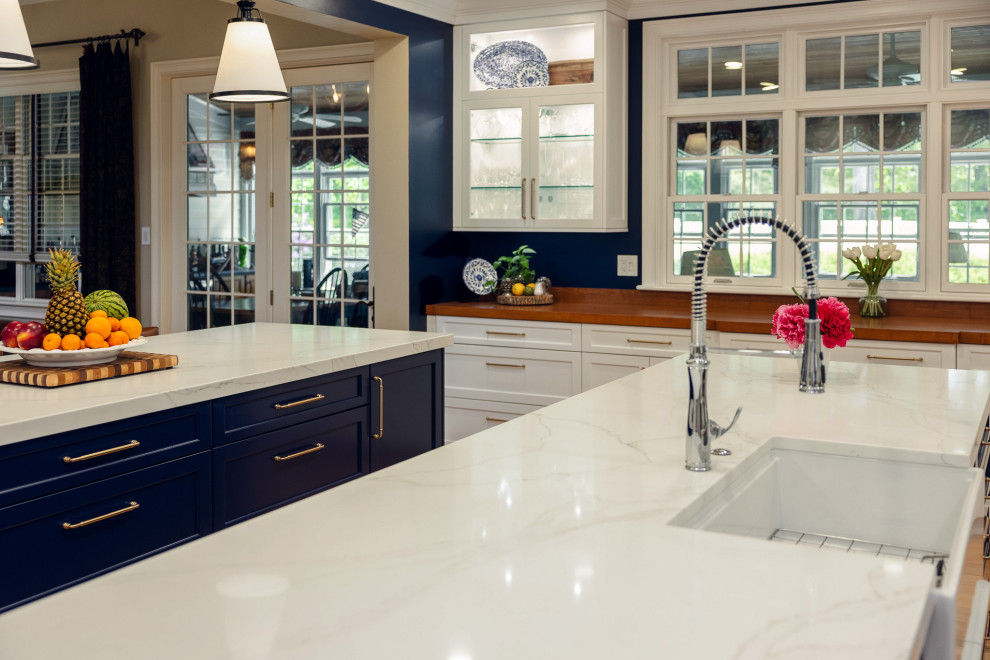 Example of a huge transitional u-shaped brown floor kitchen design with a farmhouse sink, shaker cabinets, quartz countertops, white backsplash, quartz backsplash, stainless steel appliances, two islands and white countertops