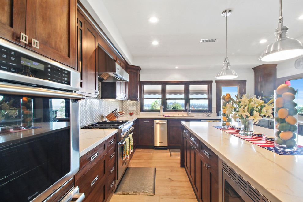 This is an example of a large midcentury u-shaped separate kitchen in Los Angeles with a single-bowl sink, shaker cabinets, dark wood cabinets, quartz benchtops, white splashback, ceramic splashback, stainless steel appliances, light hardwood floors and with island.
