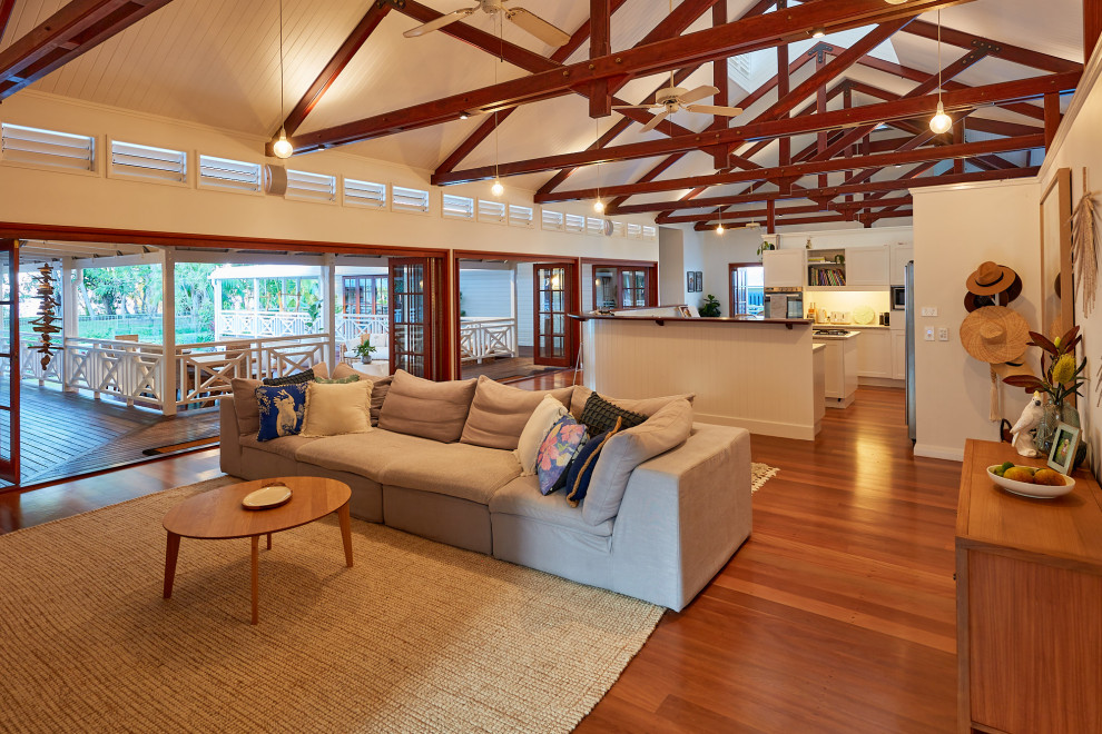 Tropical open concept living room in Cairns with white walls, medium hardwood floors, brown floor, exposed beam and vaulted.
