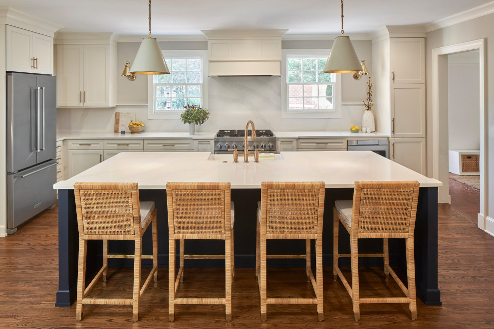 Design ideas for a large beach style l-shaped eat-in kitchen in Charlotte with a farmhouse sink, shaker cabinets, white cabinets, quartz benchtops, white splashback, engineered quartz splashback, stainless steel appliances, medium hardwood floors, with island, brown floor and white benchtop.