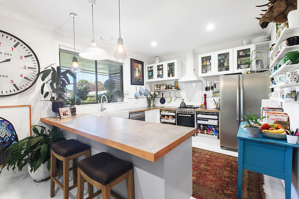 Design ideas for a mid-sized eclectic u-shaped eat-in kitchen in Melbourne with a farmhouse sink, glass-front cabinets, white cabinets, tile benchtops, white splashback, ceramic splashback, stainless steel appliances, light hardwood floors, with island, white floor and grey benchtop.
