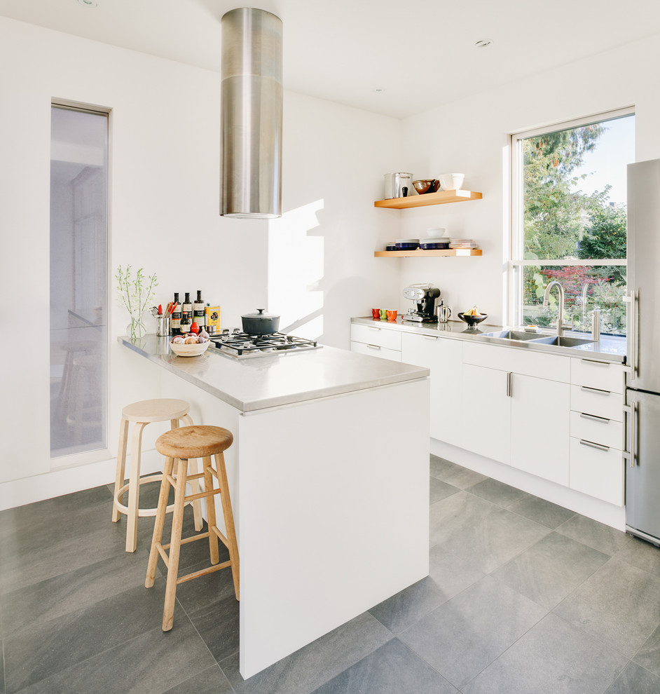 This is an example of a contemporary galley kitchen in Vancouver with ceramic floors, a double-bowl sink, flat-panel cabinets, white cabinets, window splashback, stainless steel appliances, a peninsula, grey floor and grey benchtop.