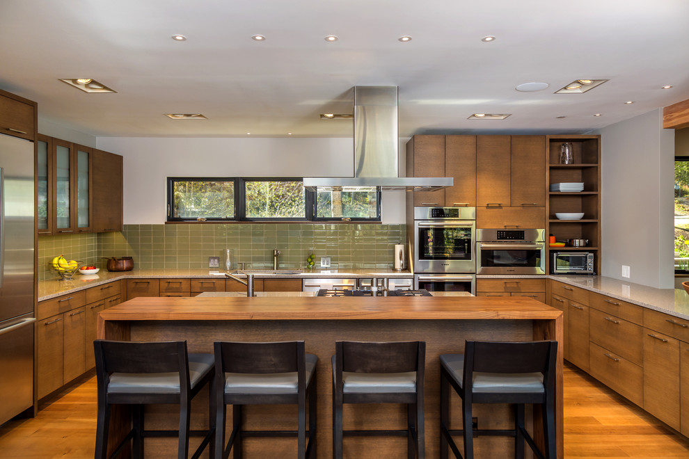 Photo of a contemporary u-shaped kitchen in Denver with flat-panel cabinets, medium wood cabinets, green splashback, stainless steel appliances, medium hardwood floors and with island.