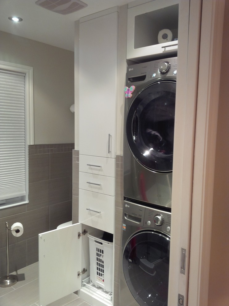 Photo of a mid-sized modern dedicated laundry room in Montreal with white cabinets, ceramic floors and a stacked washer and dryer.