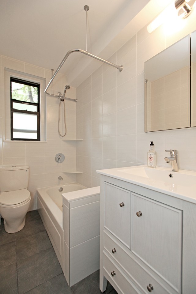 This is an example of a small traditional bathroom in New York with an undermount sink, beaded inset cabinets, white cabinets, quartzite benchtops, an alcove tub, a shower/bathtub combo, a two-piece toilet, white tile, porcelain tile, white walls and porcelain floors.