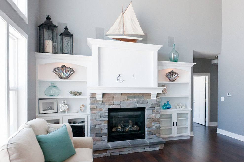 This is an example of a beach style family room in Grand Rapids with blue walls, dark hardwood floors, a standard fireplace, a stone fireplace surround and a built-in media wall.