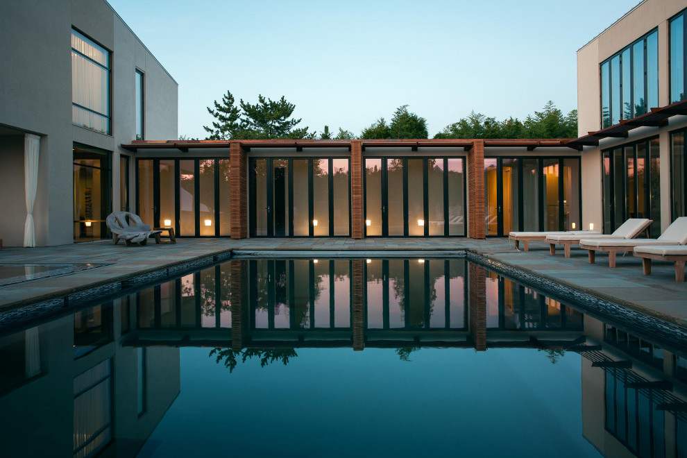 Modern backyard rectangular lap pool in New York with a pool house and concrete slab.