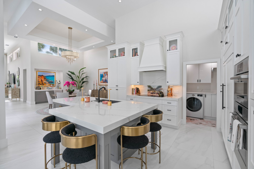 This is an example of a large transitional l-shaped eat-in kitchen in Miami with an undermount sink, shaker cabinets, white cabinets, quartz benchtops, white splashback, engineered quartz splashback, panelled appliances, porcelain floors, with island, white benchtop, vaulted and white floor.