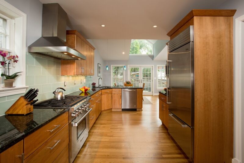 Inspiration for a mid-sized transitional u-shaped medium tone wood floor eat-in kitchen remodel in DC Metro with a single-bowl sink, flat-panel cabinets, medium tone wood cabinets, granite countertops, blue backsplash, glass tile backsplash, stainless steel appliances and a peninsula