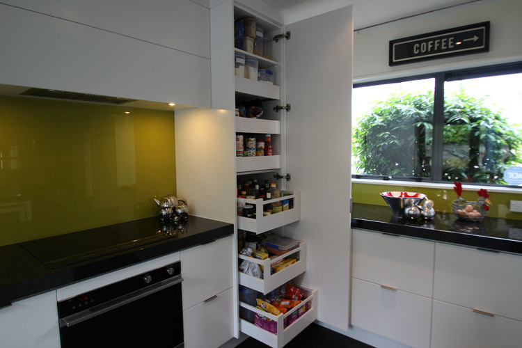 This is an example of a mid-sized contemporary u-shaped kitchen in Auckland with an undermount sink, flat-panel cabinets, white cabinets, granite benchtops, green splashback, glass sheet splashback, stainless steel appliances and ceramic floors.