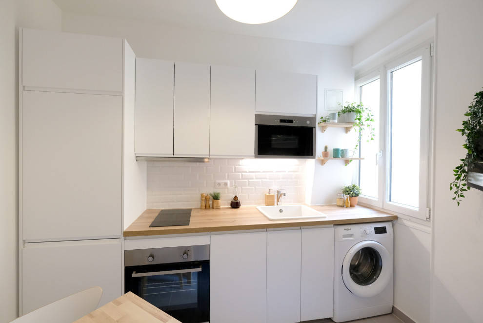 This is an example of a small scandinavian single-wall separate kitchen with an undermount sink, beaded inset cabinets, white cabinets, wood benchtops, white splashback, subway tile splashback, panelled appliances, ceramic floors, grey floor and beige benchtop.