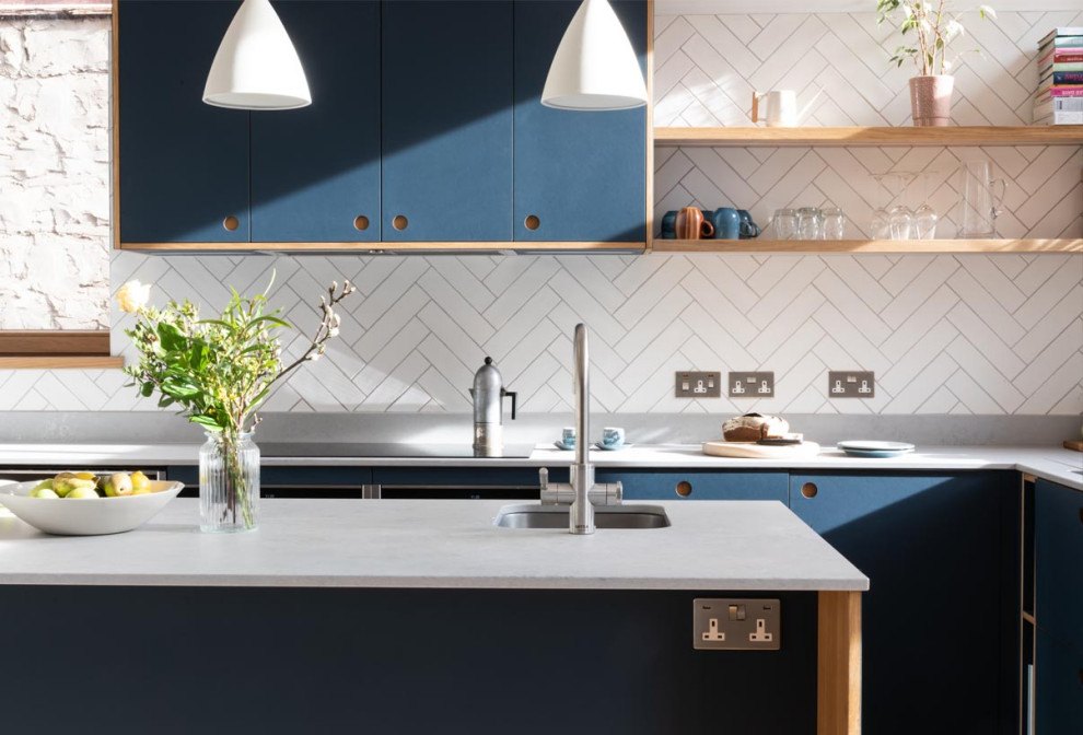 Inspiration for an expansive contemporary l-shaped open plan kitchen in London with an undermount sink, flat-panel cabinets, blue cabinets, quartzite benchtops, white splashback, ceramic splashback, black appliances, medium hardwood floors, with island, brown floor, white benchtop and vaulted.