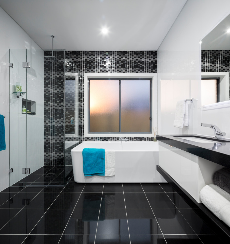 This is an example of a contemporary bathroom in Sydney with flat-panel cabinets, white cabinets, a freestanding tub, black tile, mosaic tile, an undermount sink, black floor, black benchtops, a niche and a floating vanity.