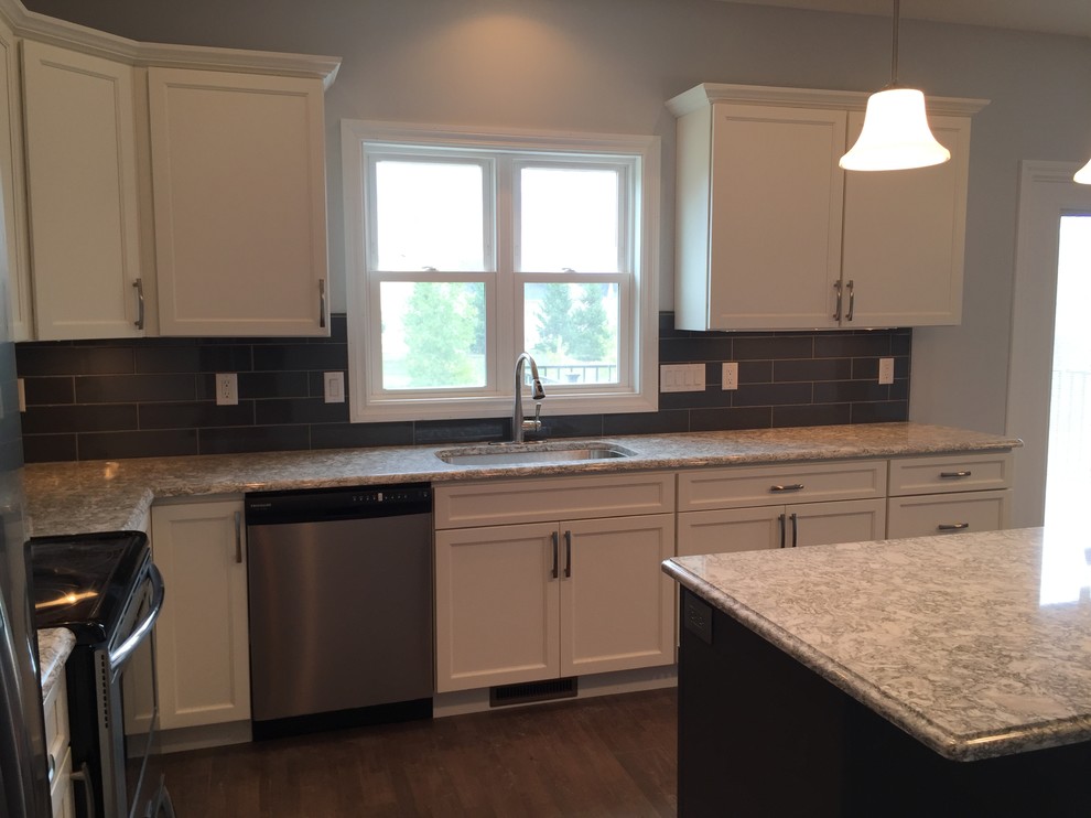 Large transitional l-shaped open concept kitchen photo with an undermount sink, raised-panel cabinets, white cabinets, quartz countertops, gray backsplash, stainless steel appliances and an island