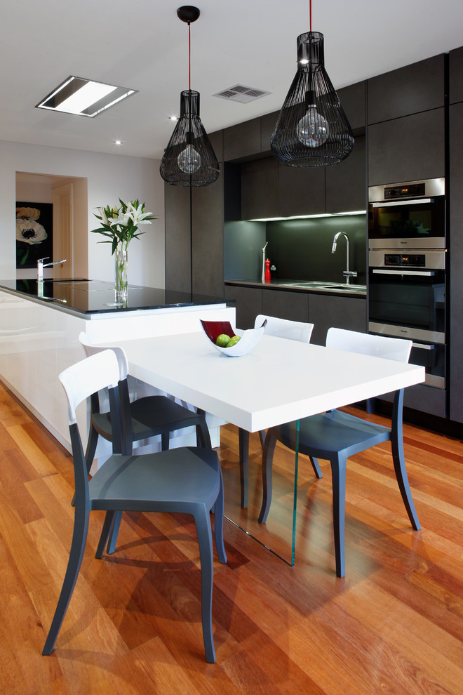 Inspiration for a mid-sized contemporary galley eat-in kitchen in Perth with an undermount sink, grey cabinets, quartz benchtops, black splashback, glass sheet splashback, stainless steel appliances, medium hardwood floors, with island and flat-panel cabinets.