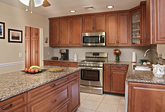 Mountain style l-shaped eat-in kitchen photo with an integrated sink, raised-panel cabinets, dark wood cabinets, quartz countertops, beige backsplash, subway tile backsplash and stainless steel appliances