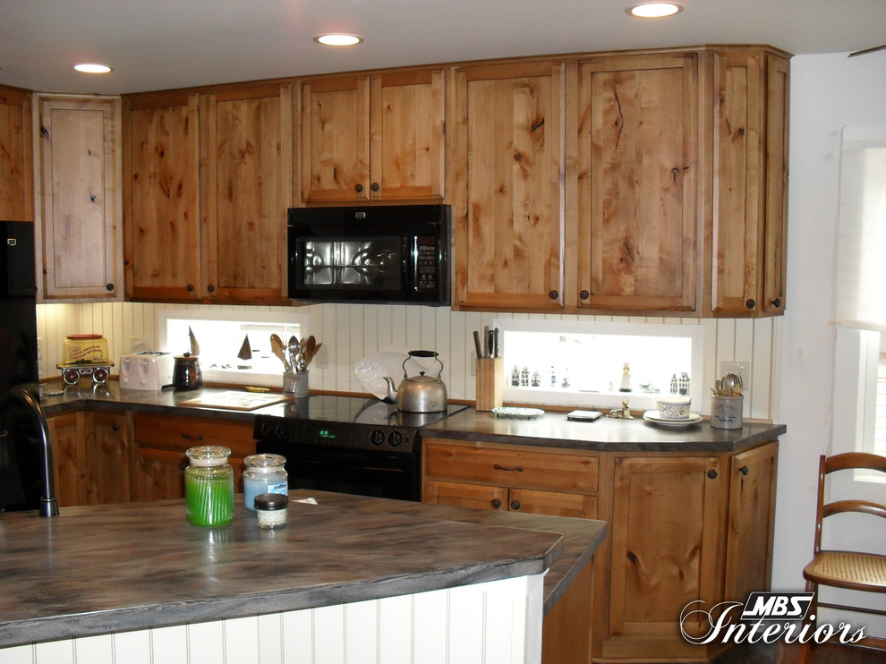 Mountain style l-shaped eat-in kitchen photo with a double-bowl sink, shaker cabinets, medium tone wood cabinets, solid surface countertops, white backsplash and black appliances
