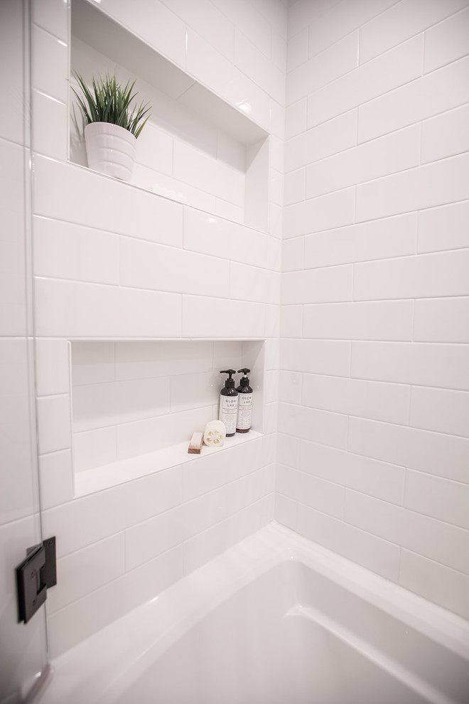 Inspiration for a small transitional 3/4 bathroom in Dallas with shaker cabinets, white cabinets, a drop-in tub, a shower/bathtub combo, a two-piece toilet, white tile, porcelain tile, white walls, limestone floors, an undermount sink, engineered quartz benchtops, black floor, a hinged shower door and white benchtops.