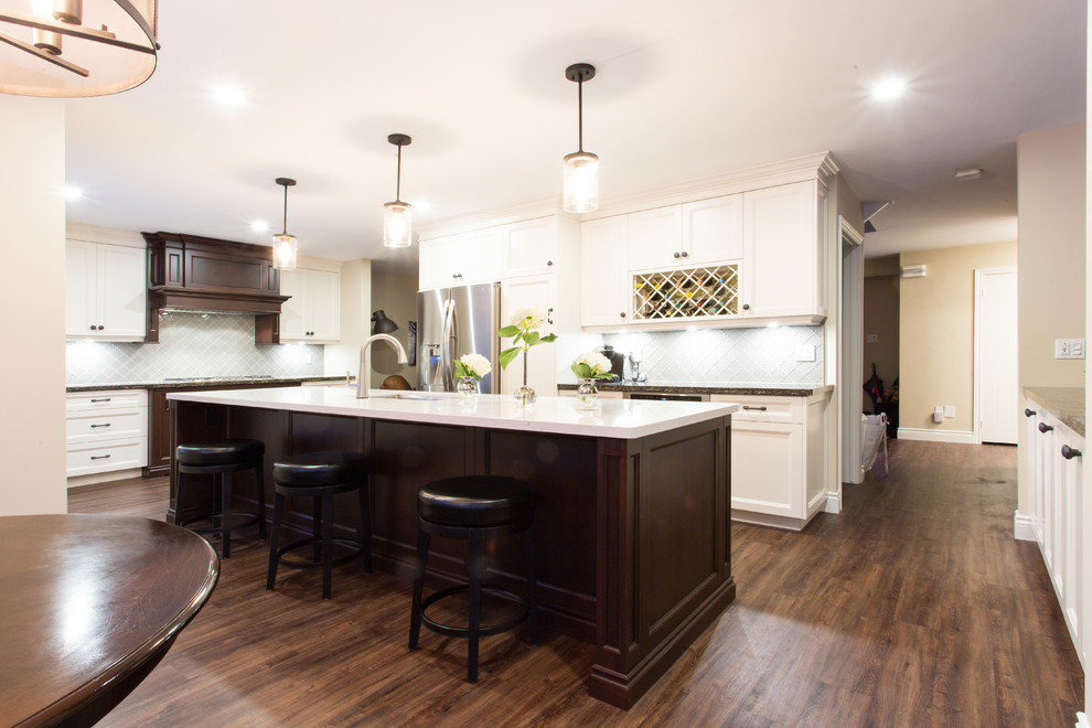 Eat-in kitchen - large transitional l-shaped dark wood floor eat-in kitchen idea in Orange County with recessed-panel cabinets, white cabinets, an island, gray backsplash, glass tile backsplash, stainless steel appliances, a double-bowl sink and granite countertops