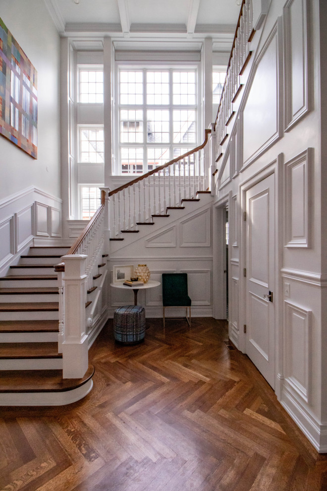 На фото: большая п-образная лестница в классическом стиле с деревянными ступенями, крашенными деревянными подступенками, деревянными перилами и панелями на части стены