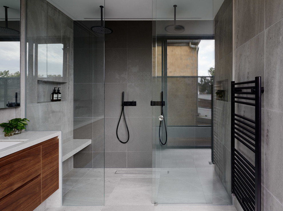 Inspiration for a mid-sized contemporary master bathroom in Melbourne with flat-panel cabinets, medium wood cabinets, a double shower, a one-piece toilet, gray tile, ceramic tile, grey walls, ceramic floors, an undermount sink, engineered quartz benchtops, grey floor and a sliding shower screen.
