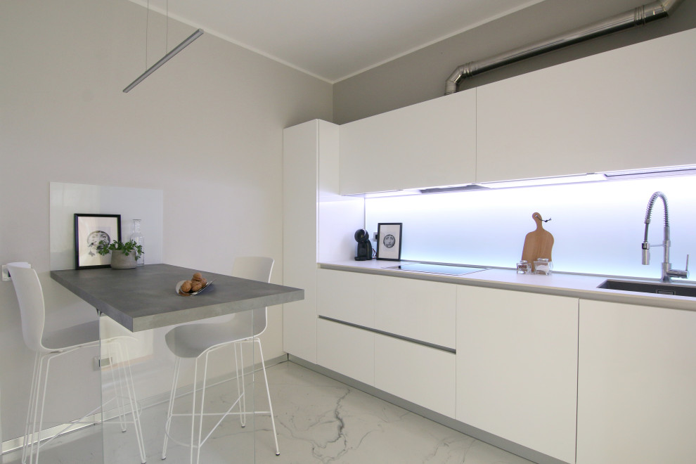 Mid-sized contemporary galley separate kitchen in Milan with an integrated sink, flat-panel cabinets, white cabinets, white splashback, glass sheet splashback, black appliances, a peninsula, white floor and beige benchtop.