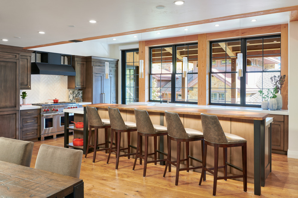 Design ideas for a country l-shaped open plan kitchen in Denver with shaker cabinets, medium wood cabinets, white splashback, stainless steel appliances, medium hardwood floors, with island, brown floor and white benchtop.