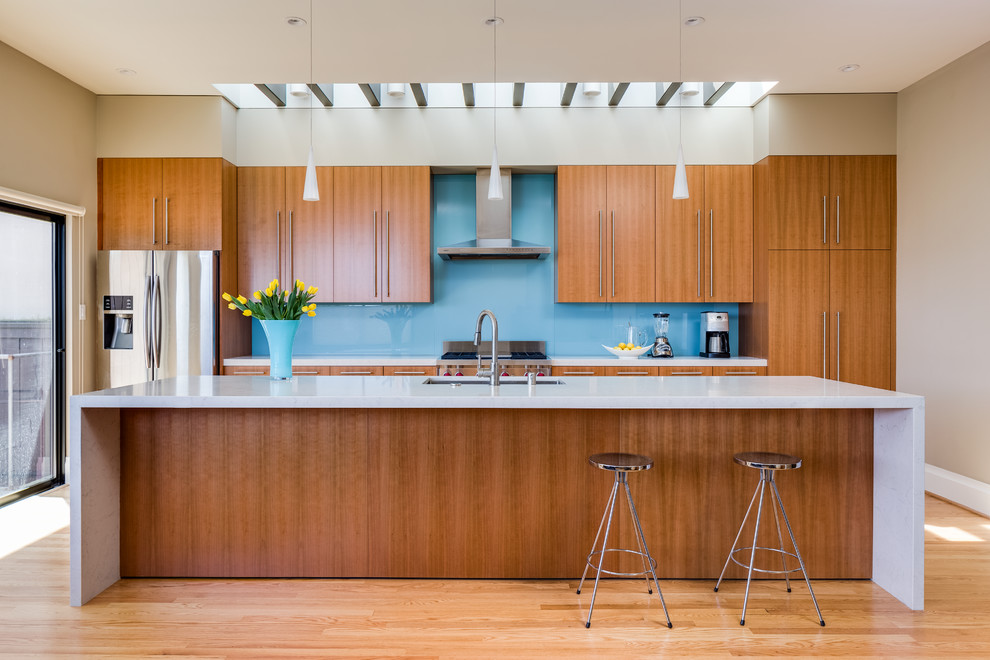 Design ideas for a mid-sized contemporary galley open plan kitchen in San Francisco with an undermount sink, flat-panel cabinets, medium wood cabinets, quartz benchtops, blue splashback, glass sheet splashback, stainless steel appliances, light hardwood floors and with island.