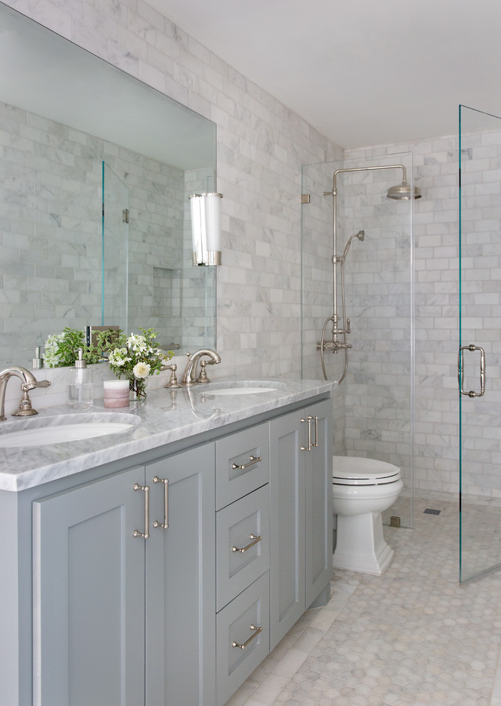 Photo of a small traditional bathroom in Austin with shaker cabinets, blue cabinets, a curbless shower, a one-piece toilet, gray tile, marble, marble floors, an undermount sink, marble benchtops, grey floor, a hinged shower door and grey benchtops.
