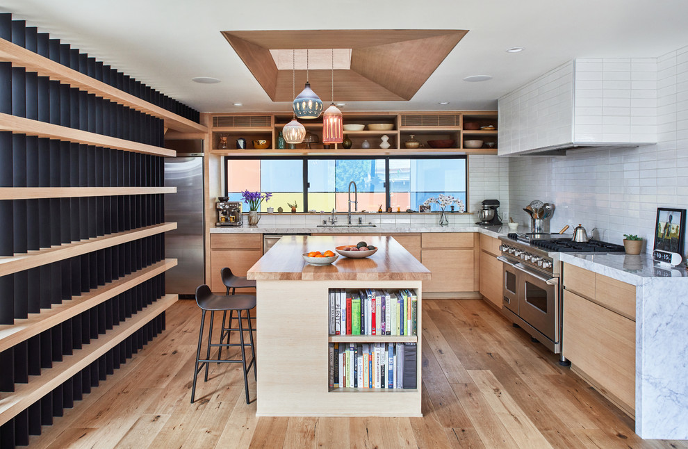 This is an example of a large contemporary l-shaped kitchen in Los Angeles with a double-bowl sink, light wood cabinets, marble benchtops, white splashback, ceramic splashback, stainless steel appliances, light hardwood floors, with island, beige floor, white benchtop and flat-panel cabinets.