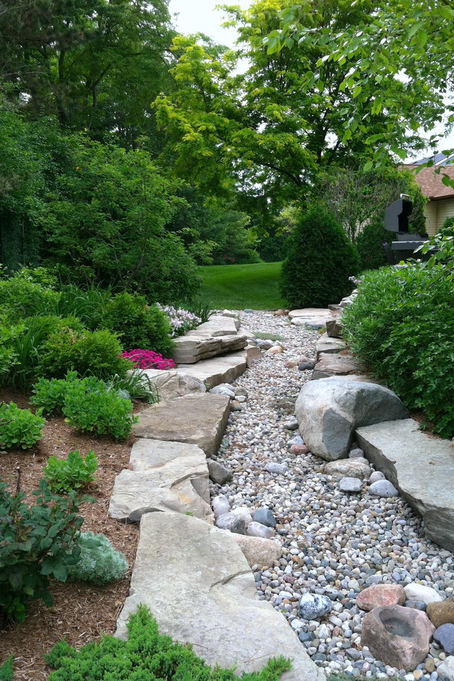 Small country backyard full sun xeriscape in Detroit with natural stone pavers and a retaining wall for summer.