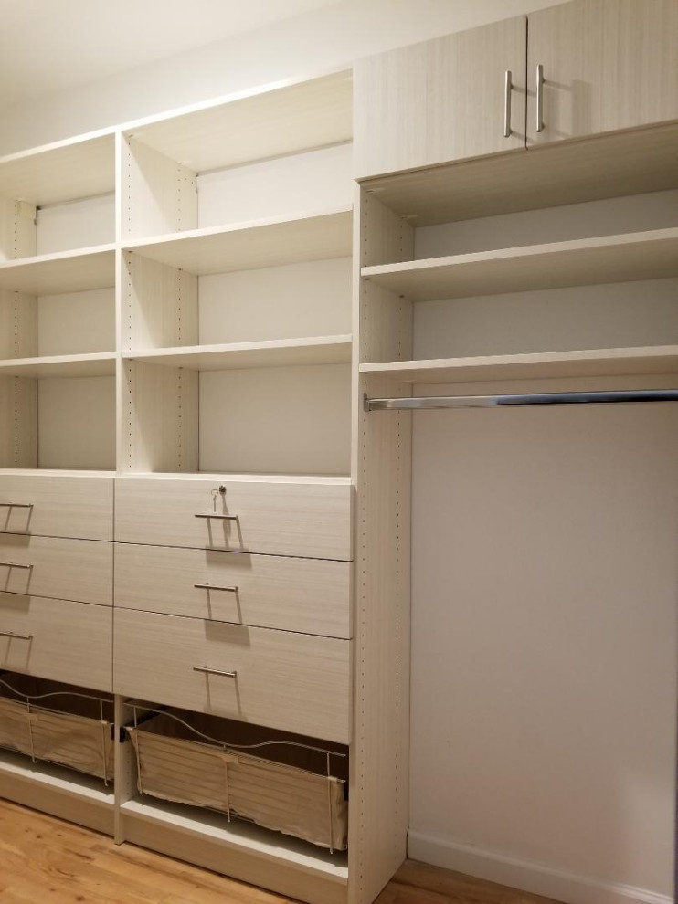 Photo of an expansive modern gender-neutral walk-in wardrobe in New York with flat-panel cabinets, light wood cabinets, light hardwood floors, beige floor and vaulted.